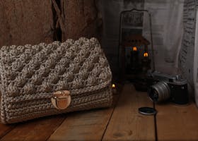 Elegant knitted bag and vintage camera placed on wooden surface with warm, ambient lighting.